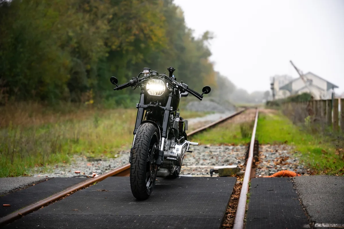 Moto rétro noire stationnée sur une ancienne voie ferrée en automne.