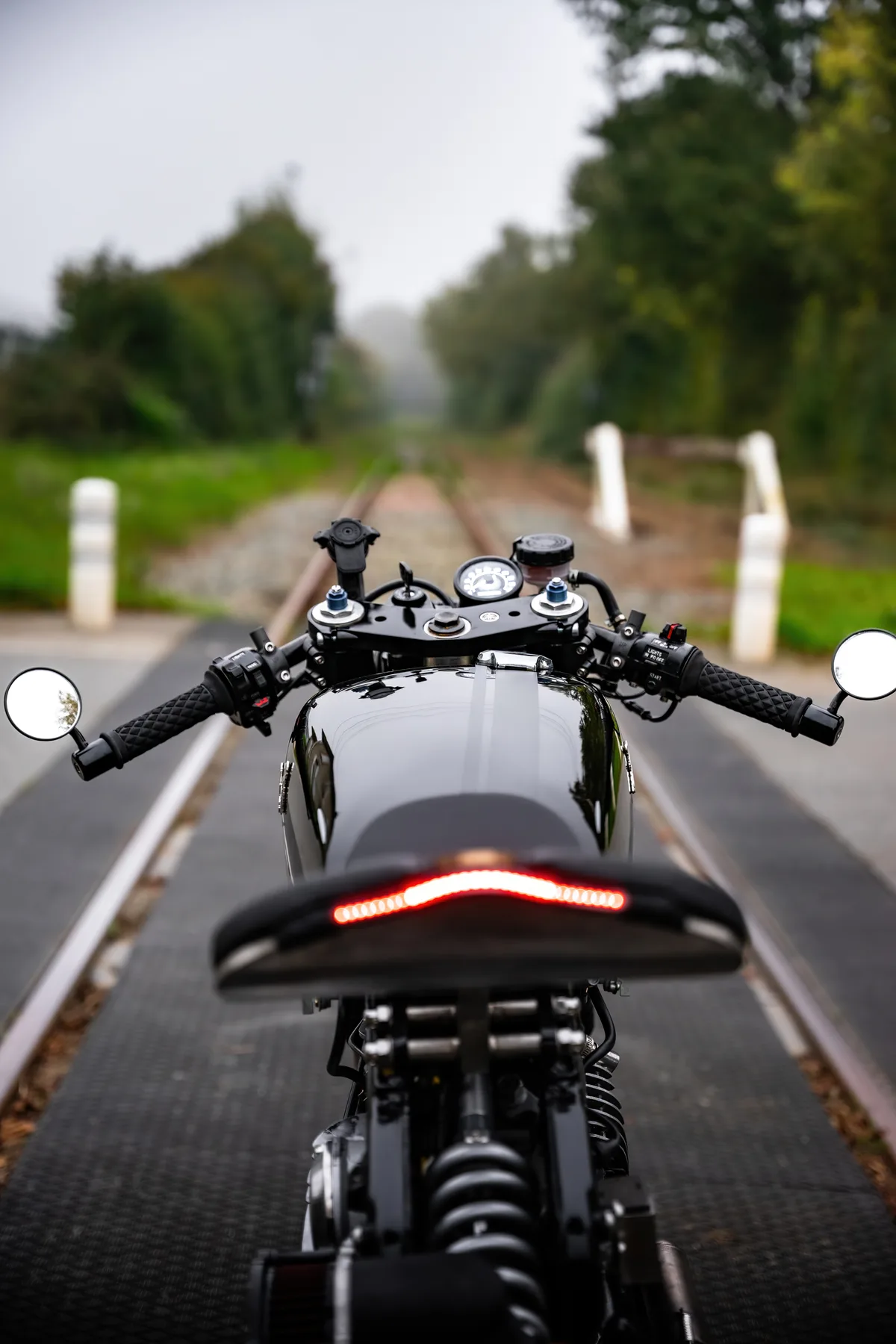 Vue arrière d’une moto rétro stationnée sur une route bordée d’arbres.