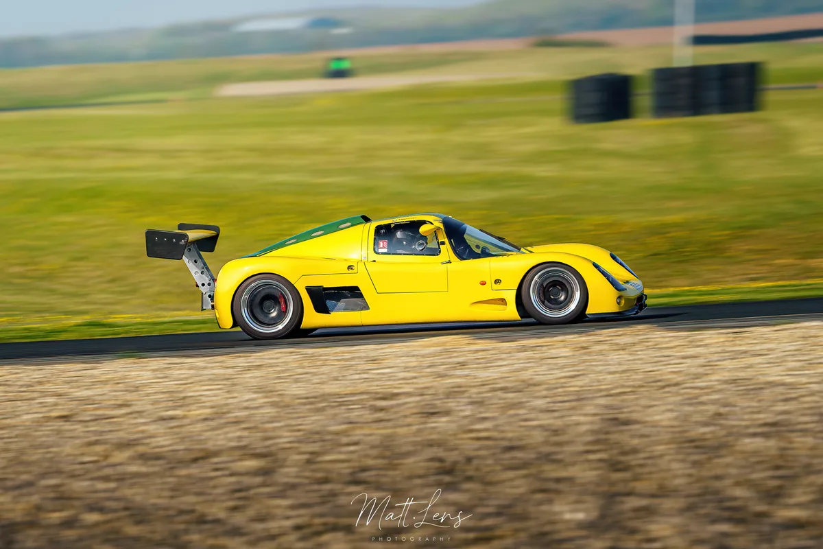La voiture de course jaune accélère sur le circuit.