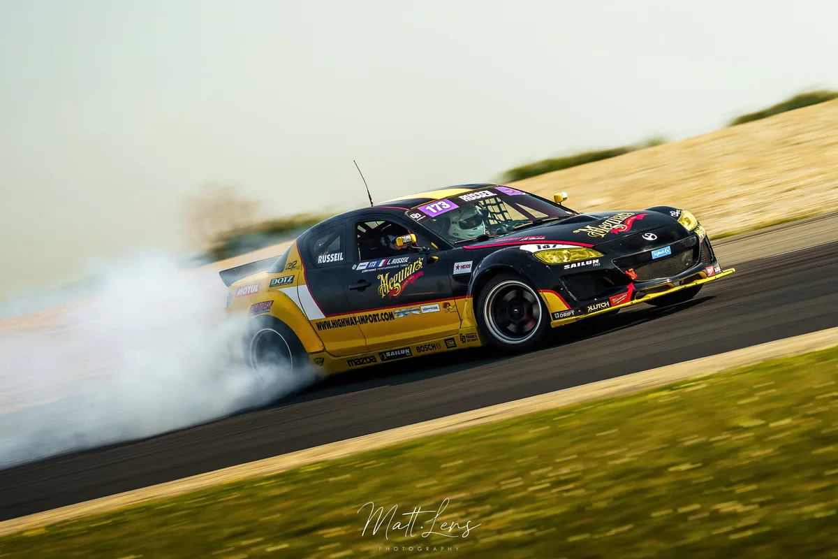 La voiture de course noire dérive sur la piste dans un nuage de fumée.