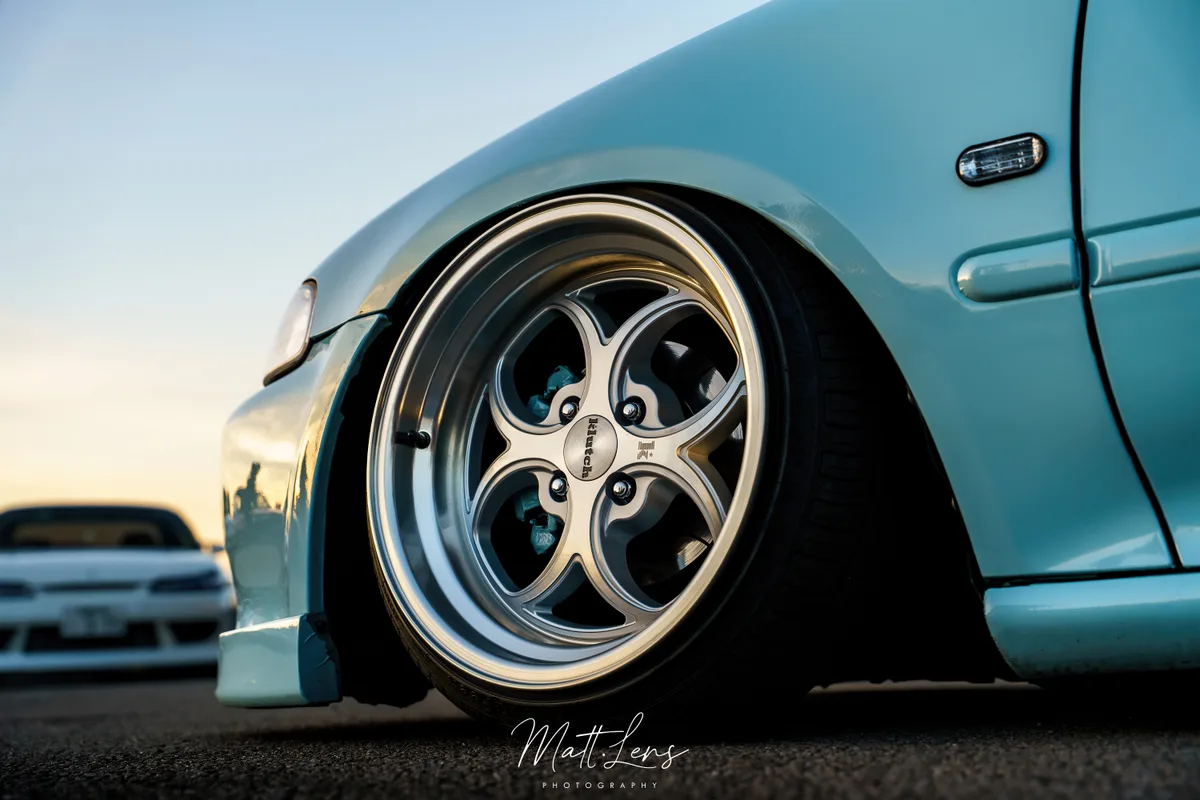 Détail d’une jante chromée sur une voiture bleu turquoise.