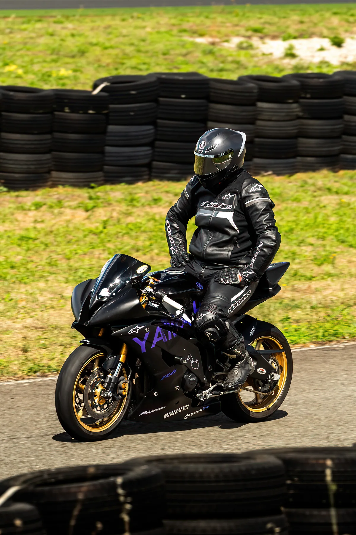 Un motard en équipement noir pose sur sa moto près des pneus de piste.