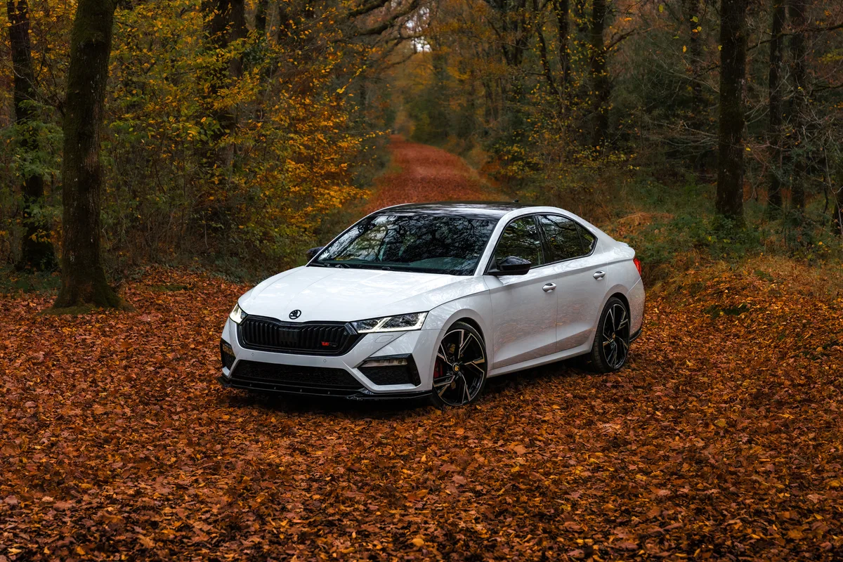 La Skoda blanche roule sur une route couverte de feuilles d’automne.
