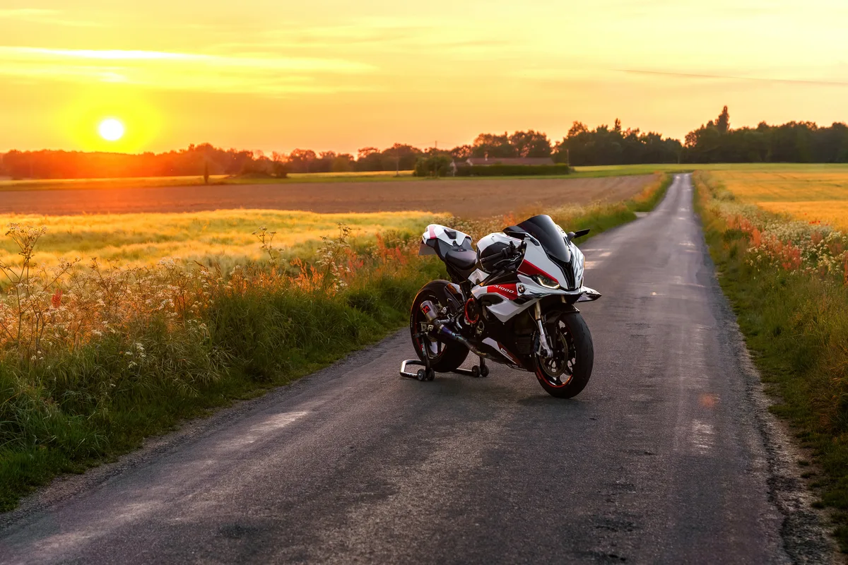 Un motard s’arrête avec sa moto sportive dans la lumière du coucher de soleil.