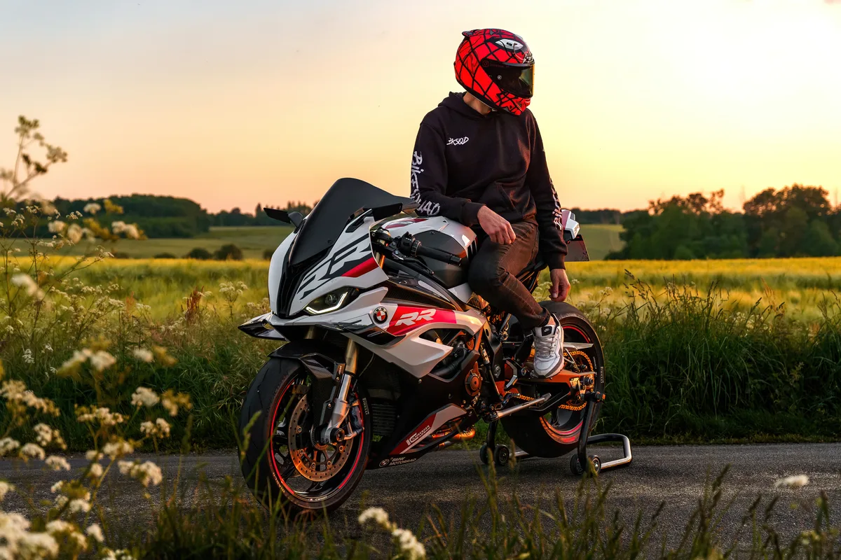 Portrait d’une moto rouge et noire garée au coucher du soleil.
