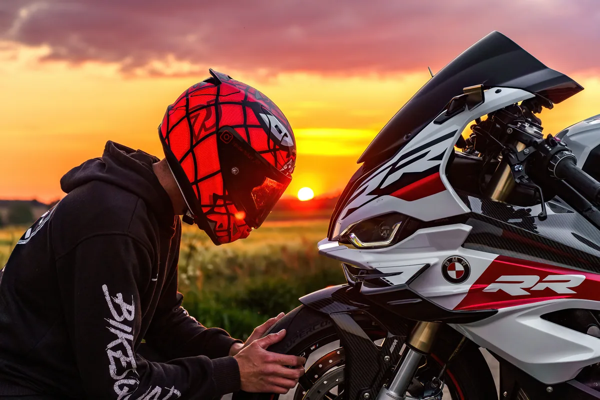 Le motard ajuste son casque près de sa moto dans la lumière du soir.
