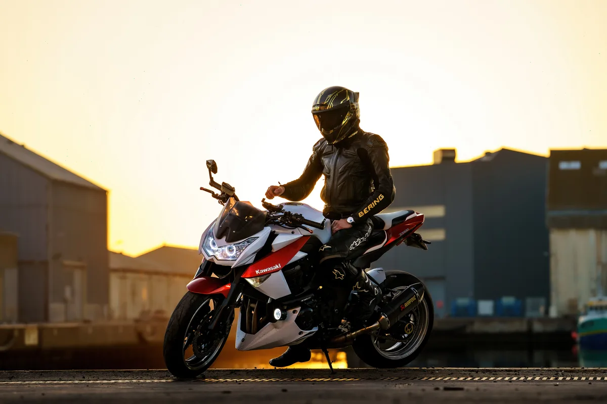 Un motard prend place sur sa moto sportive devant le soleil couchant.