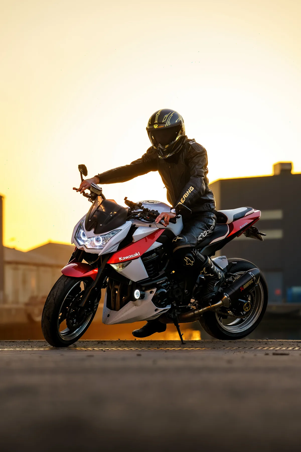 Portrait vertical d’un motard assis sur sa moto au soleil couchant.