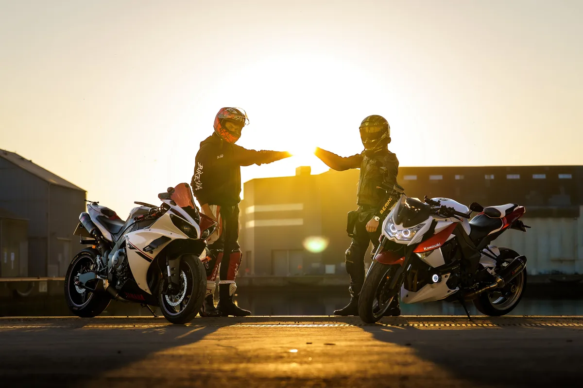 Deux motards et leurs motos en silhouette devant le soleil couchant.
