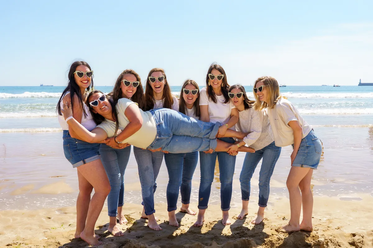 Les amies prennent la pose en riant sur le sable, face à l’océan.
