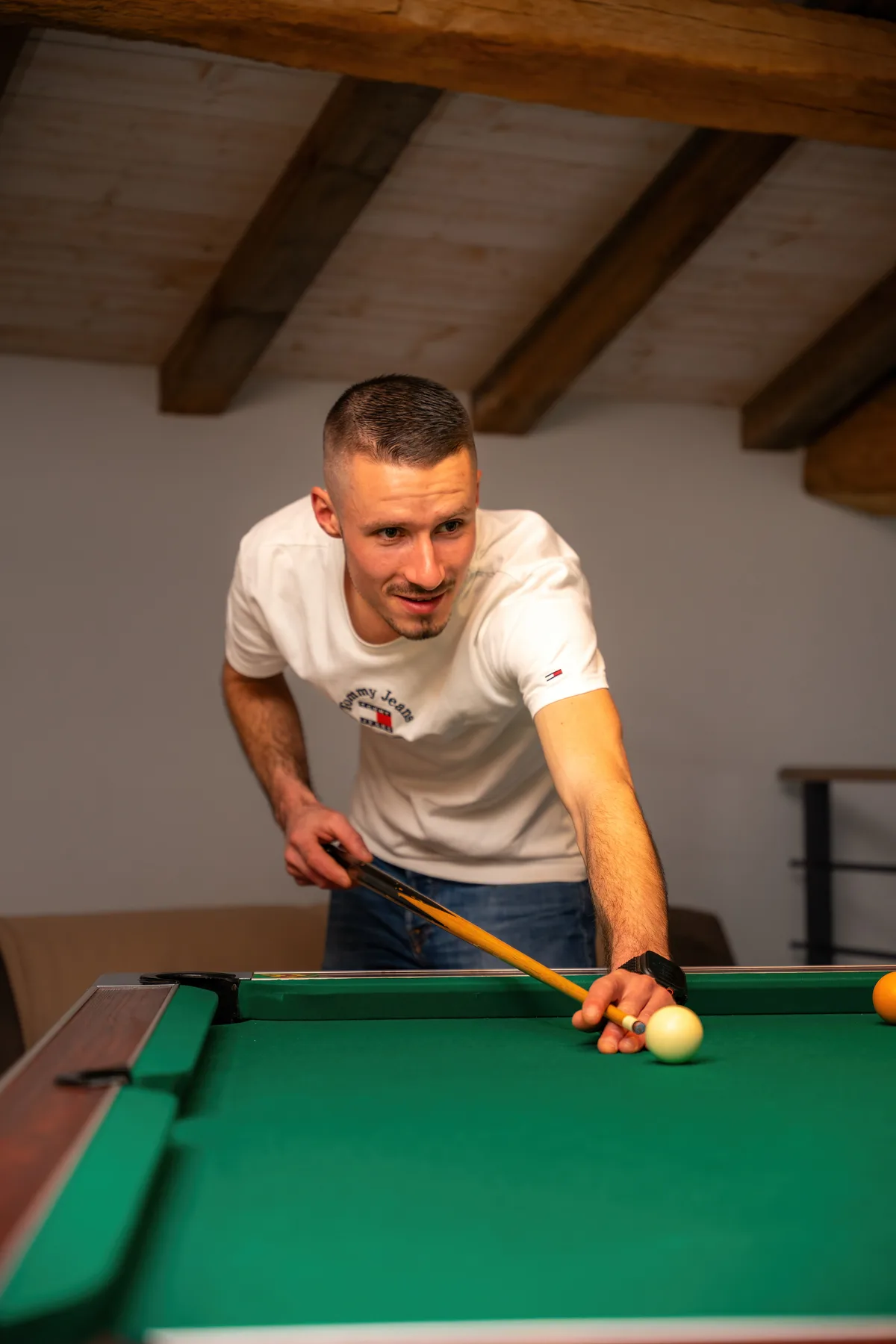 Un homme joue au billard dans une salle aux poutres apparentes.