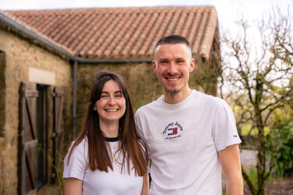 Portrait d’un couple devant une maison en pierre, dans le jardin.