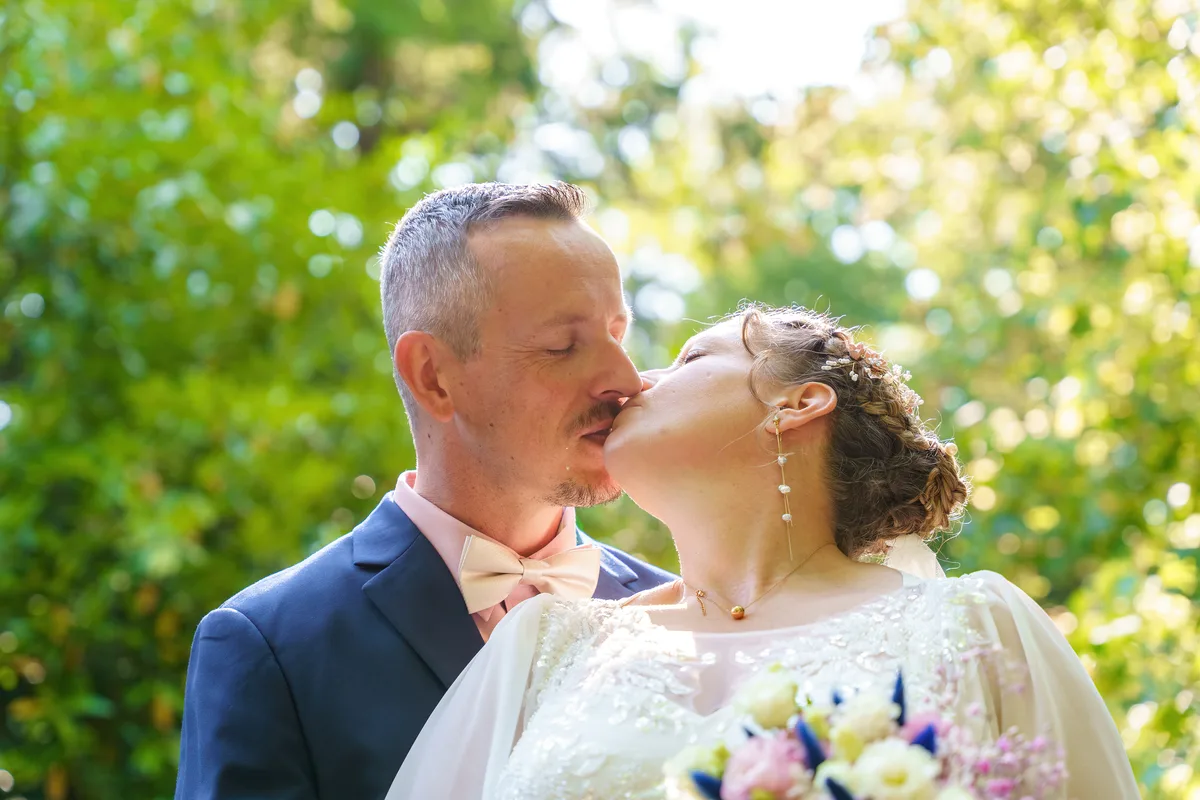 Les mariés échangent un baiser, le bouquet de la mariée au premier plan.