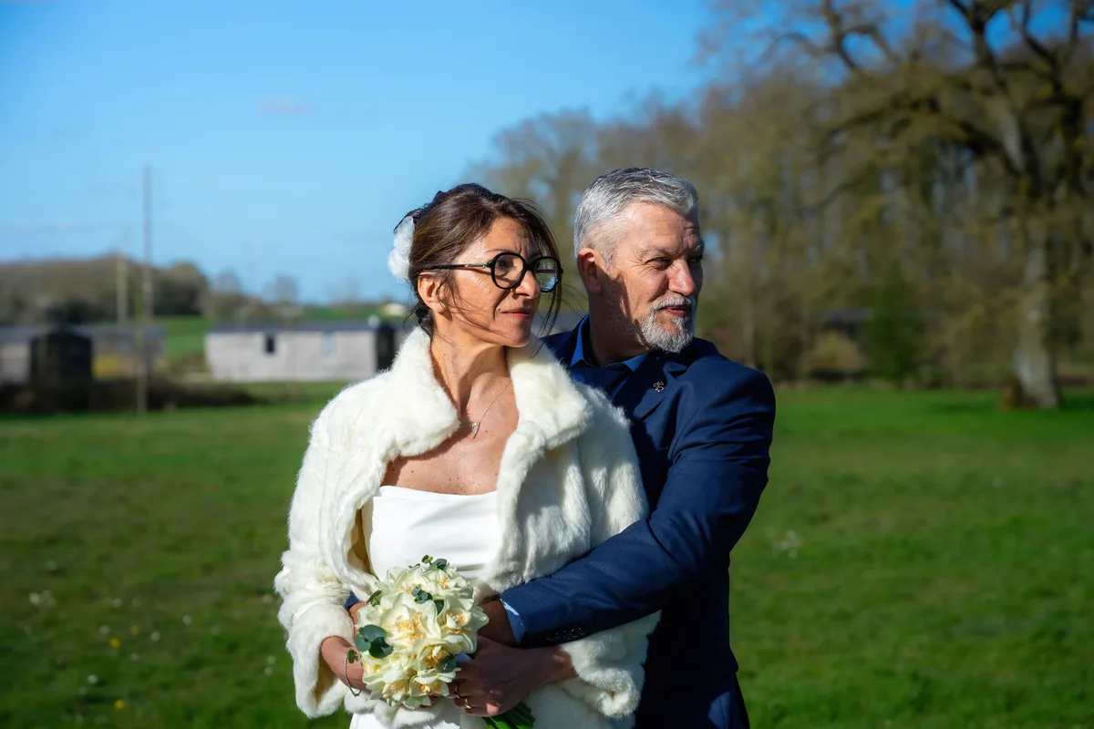 Le marié enlace la mariée qui tient son bouquet dans le jardin.