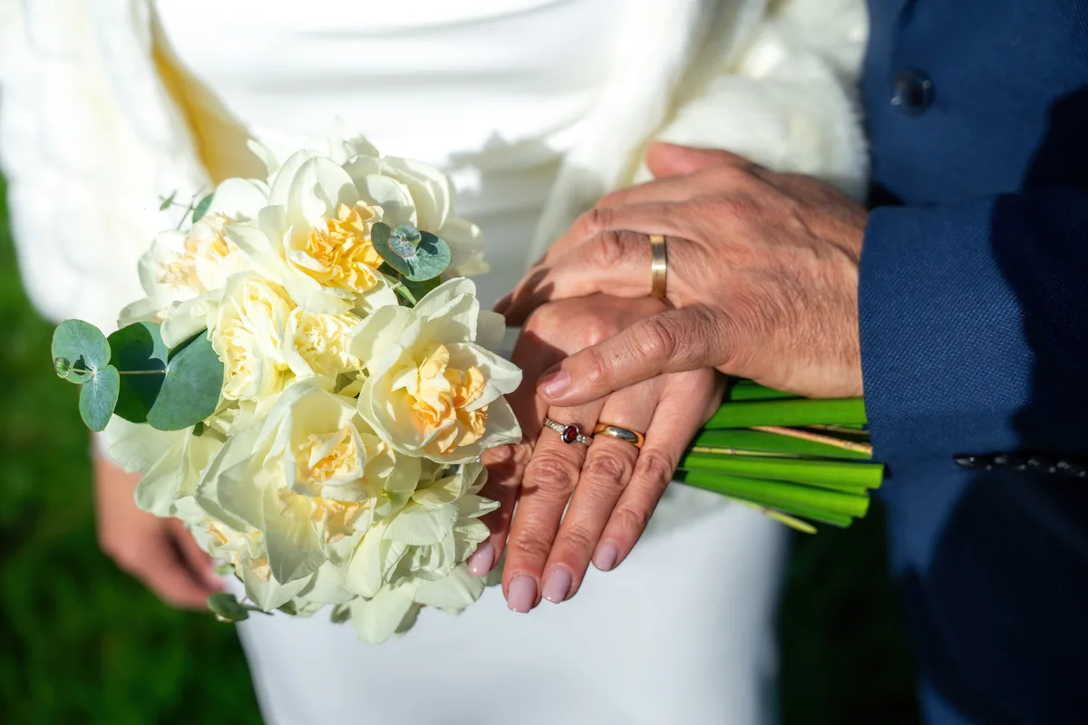 Gros plan sur le bouquet de mariée et les mains qui le tiennent.