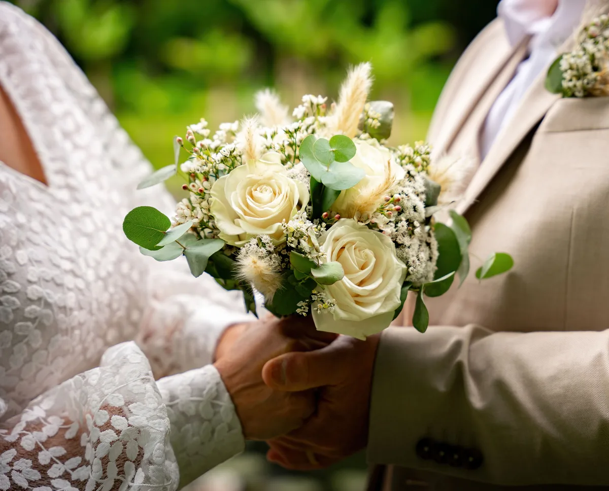 Gros plan sur le bouquet et les mains des mariés.