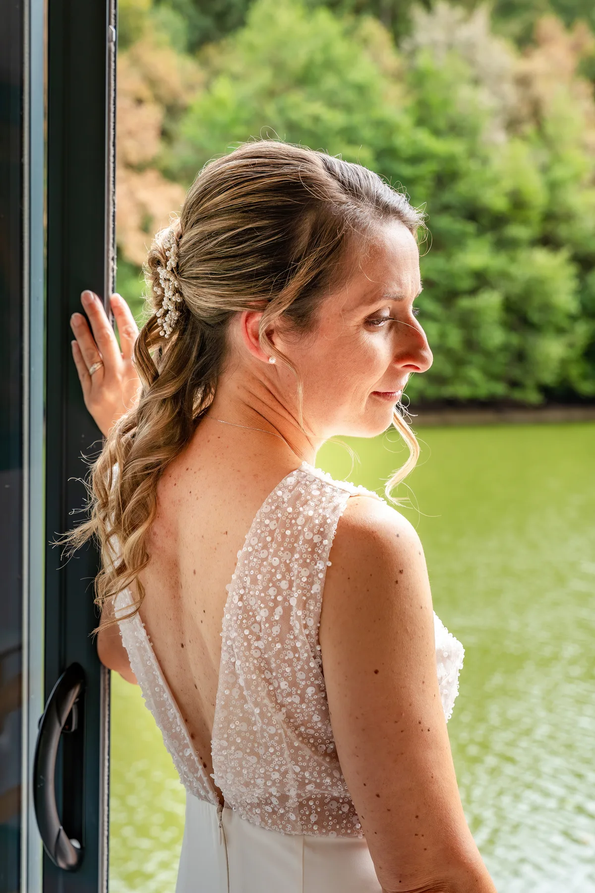 Portrait de la mariée en robe de dentelle près d’une fenêtre ouverte sur le jardin.