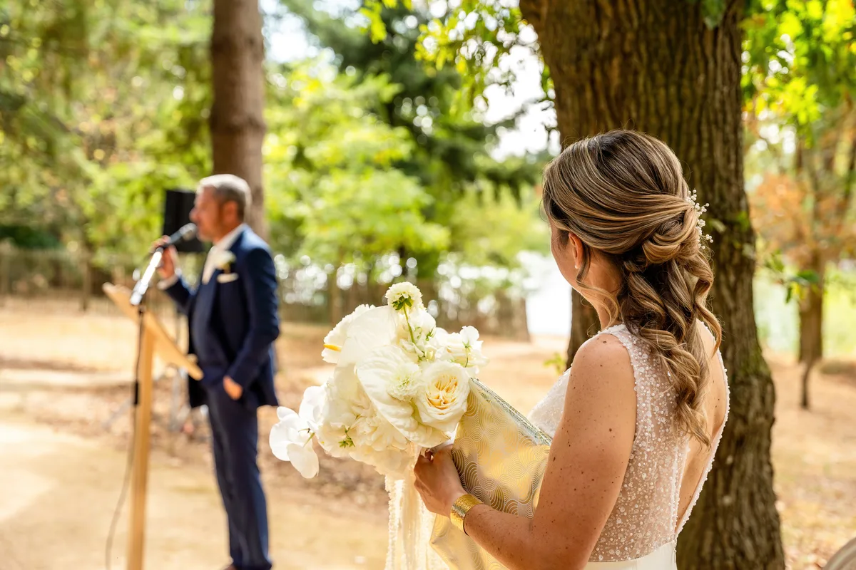 La mariée, bouquet à la main, regarde le marié qui l’attend sous l’arche.