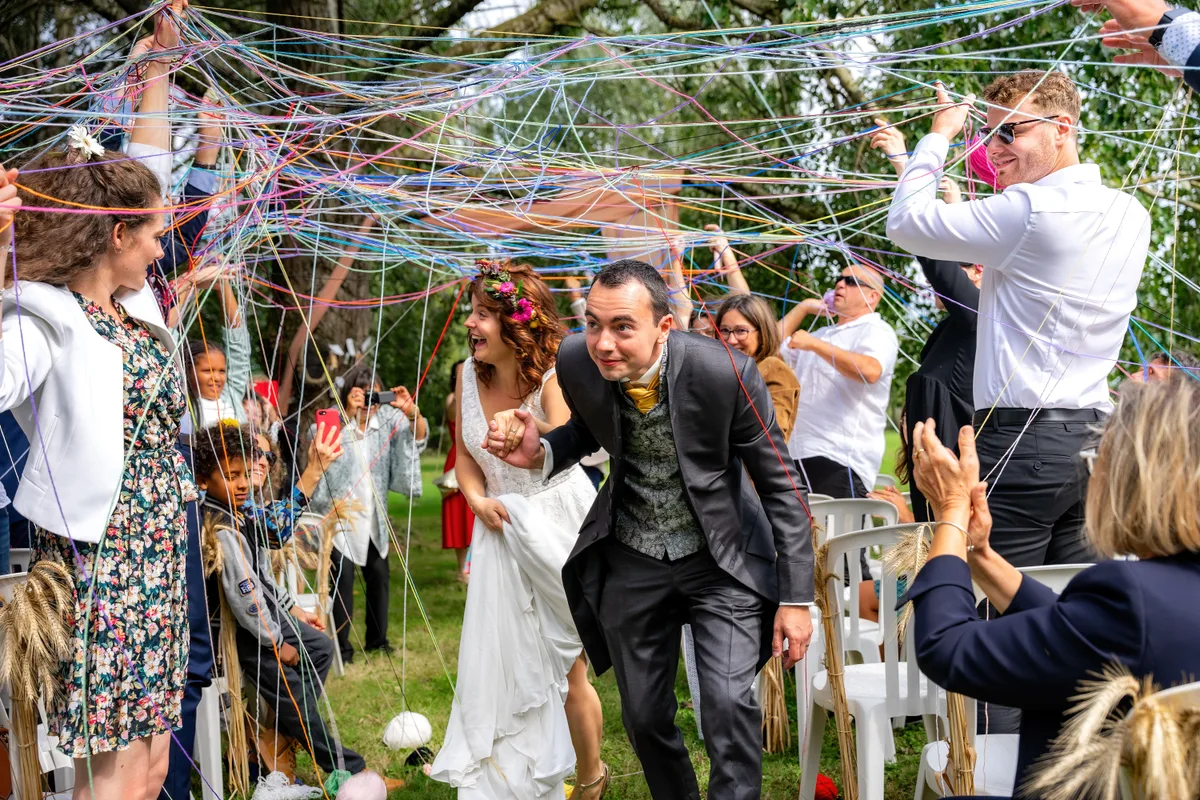 Les mariés traversent une haie d’honneur sous les rubans lancés par les invités.