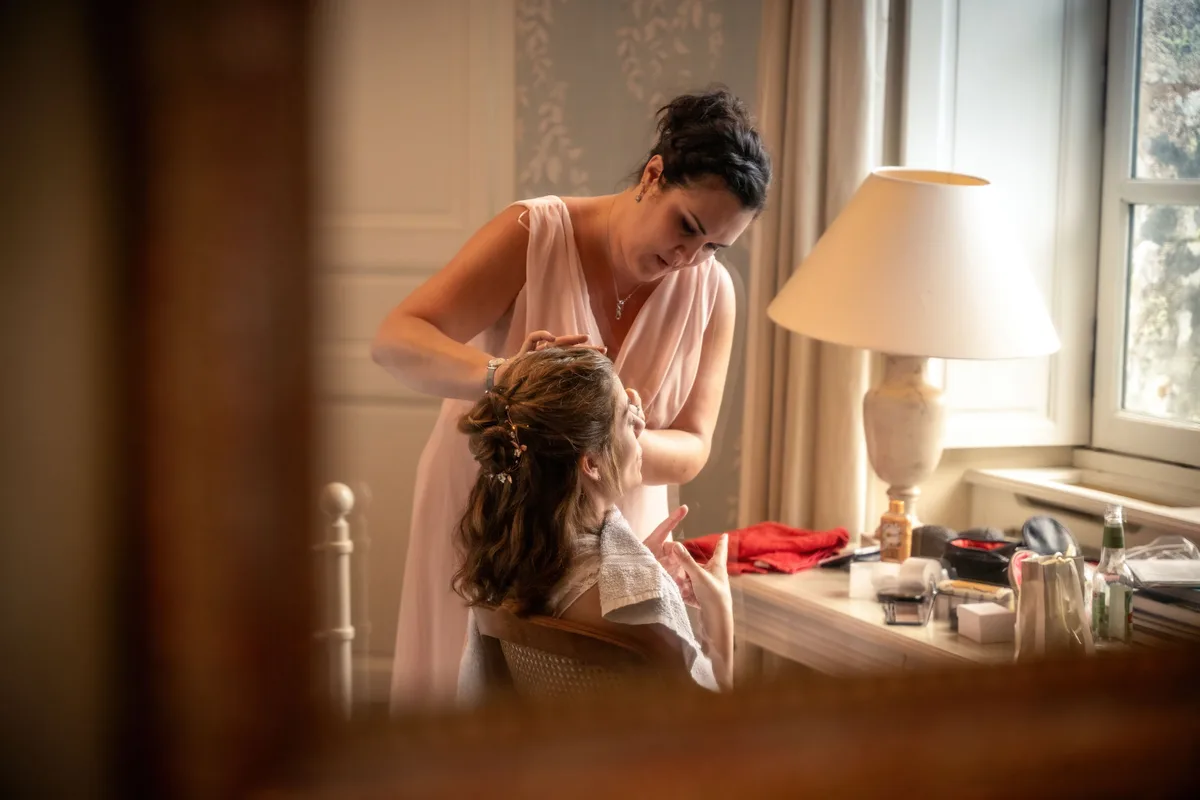 La mariée se prépare près d’une fenêtre, bouquet à la main.