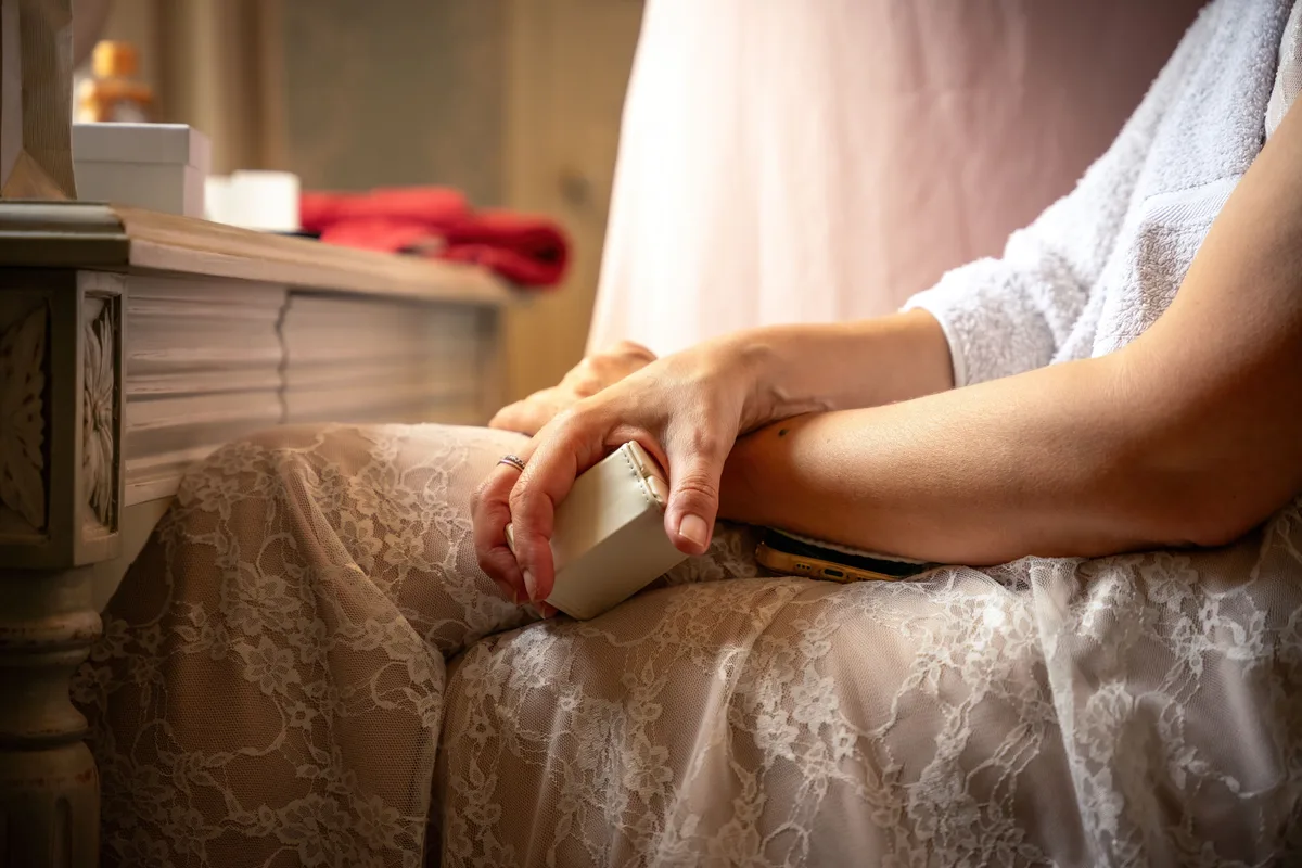 Détail des préparatifs de la mariée, assise près d’une fenêtre avant la cérémonie.