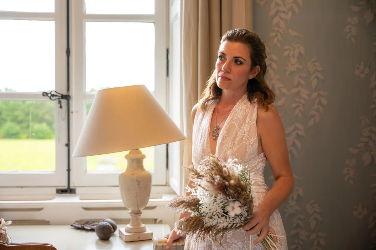 Portrait de la mariée près d’une fenêtre, son bouquet dans les mains.