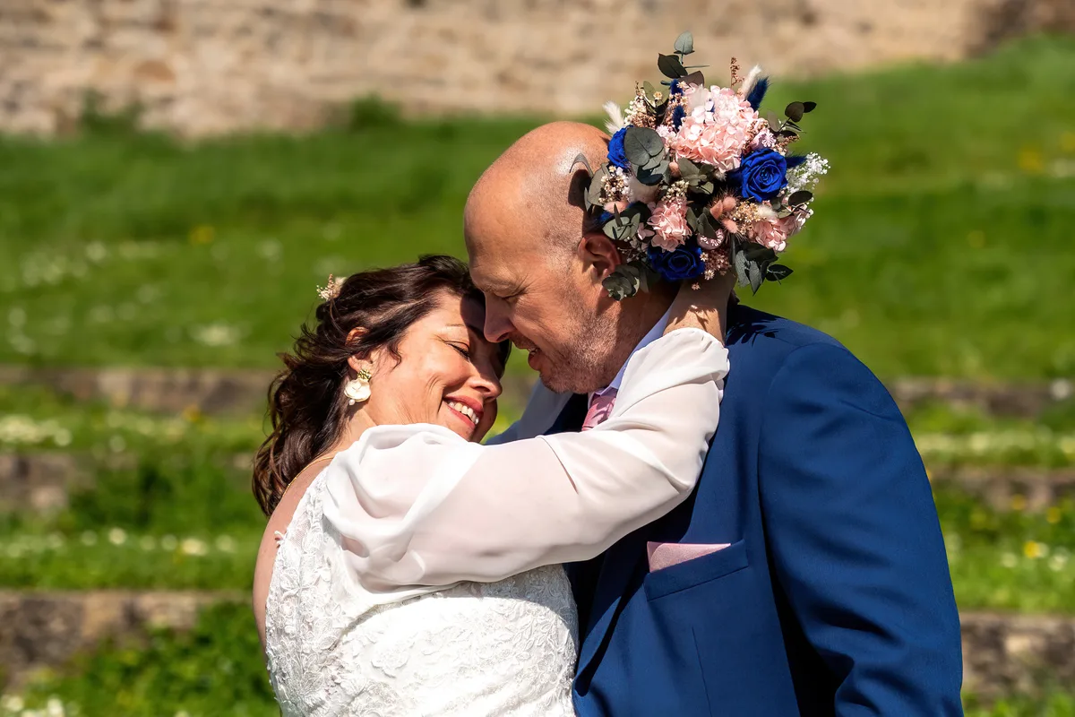 Le marié embrasse la mariée qui tient son bouquet devant le jardin.