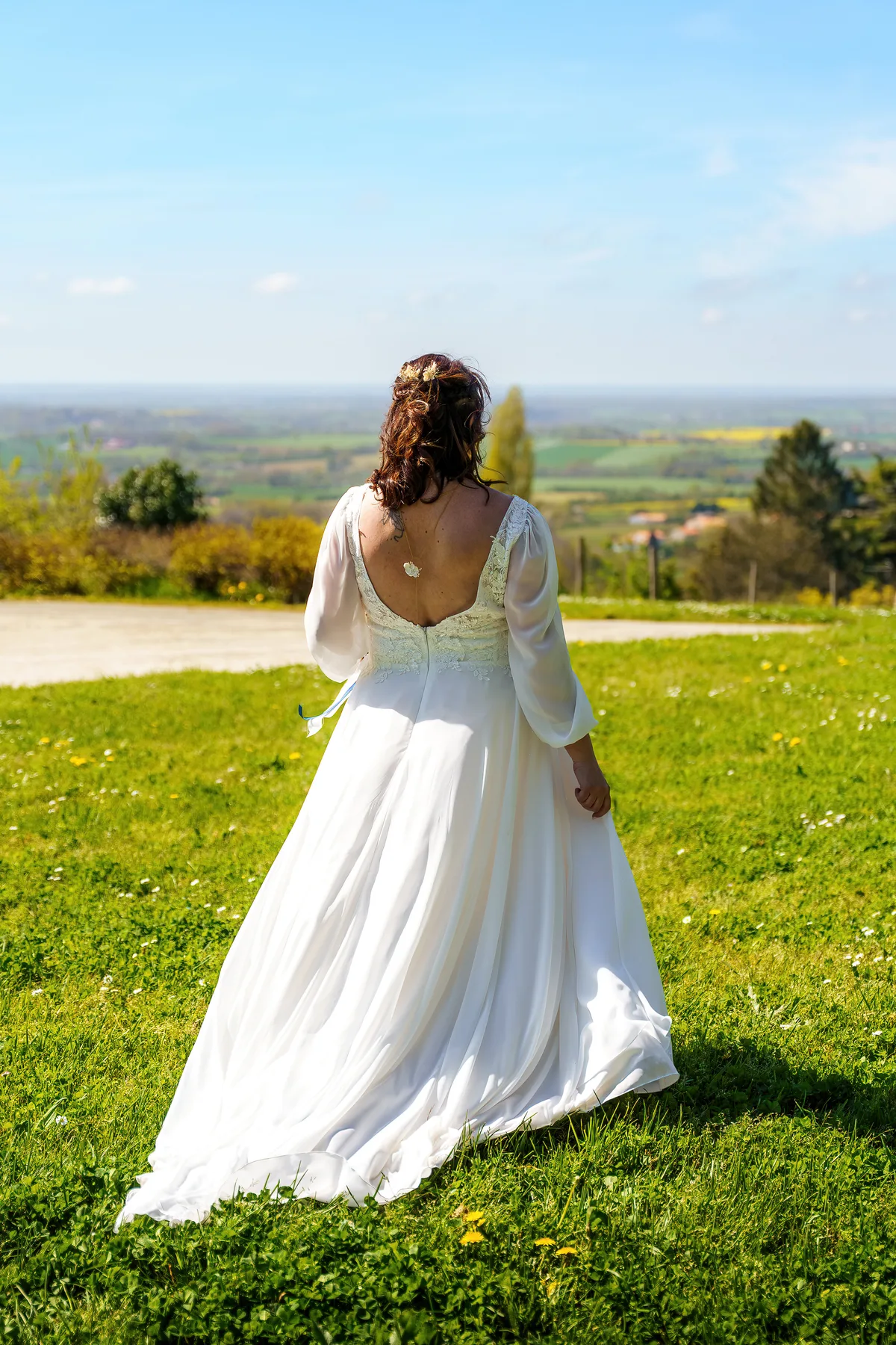 La mariée pose seule en robe blanche face au paysage.