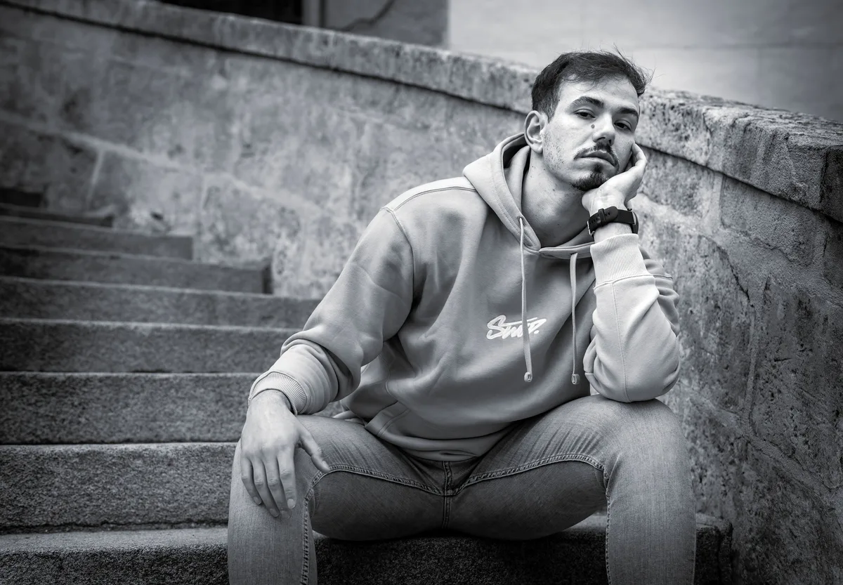 Portrait de Mohamed assis sur un escalier, vêtu d’un sweat.