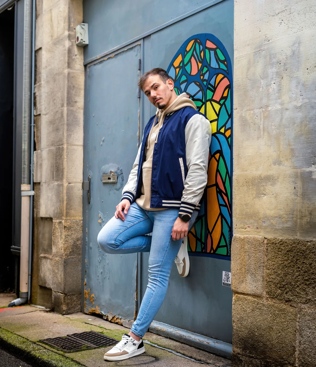 Mohamed pose devant une fresque colorée dans une rue.