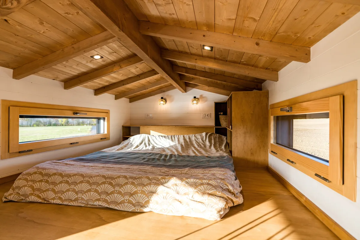 Lit et espace nuit aménagés sous le toit en bois de la tiny house.